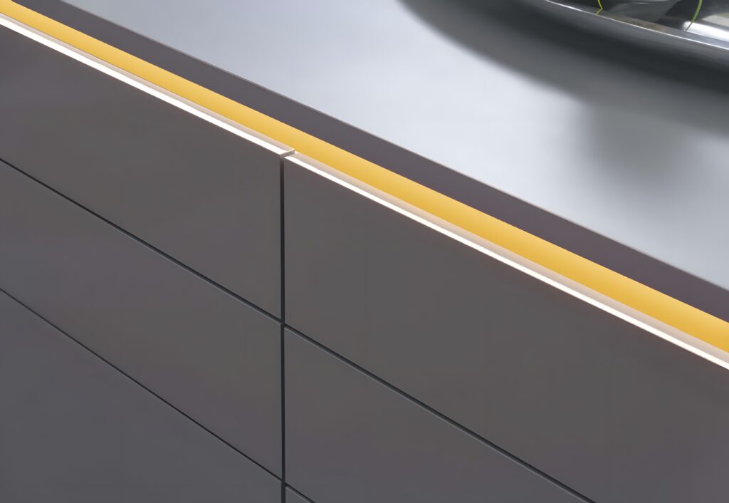 Close-up of a modern kitchen cabinet with high gloss finish, minimalist handle-less design, and integrated yellow LED lighting running along the top edge.