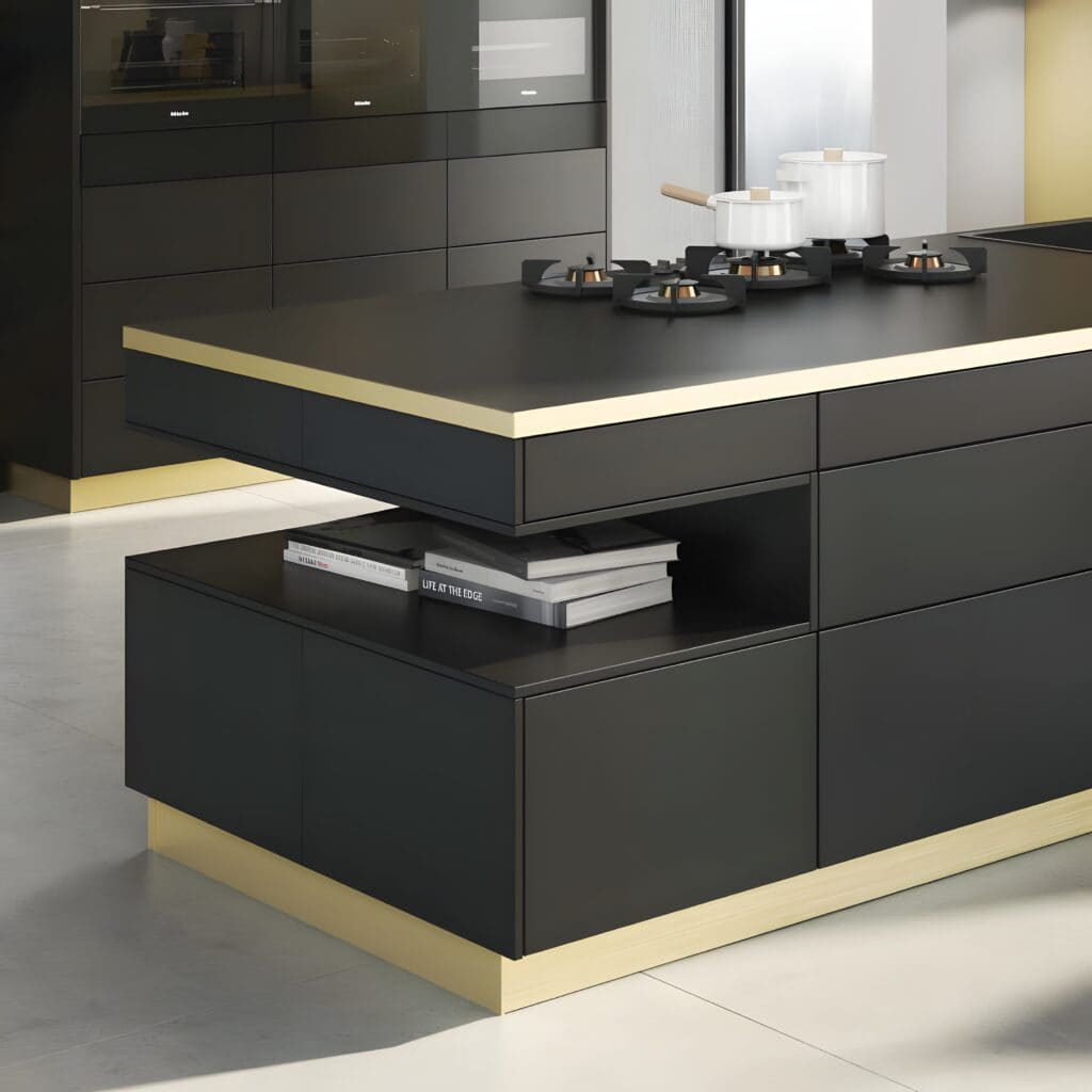 A modern kitchen island with a black matte finish and gold trim, featuring a built-in gas cooktop with four burners. Below the countertop, there are sleek German kitchen cabinets and storage shelves with a few books.