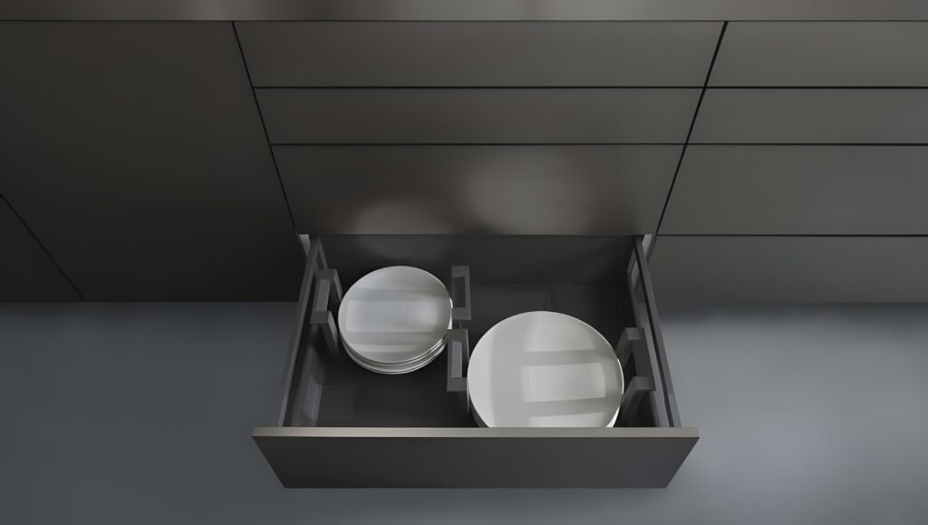 Open kitchen drawer containing neatly stacked white plates against a backdrop of modern, grey German kitchen cabinets.