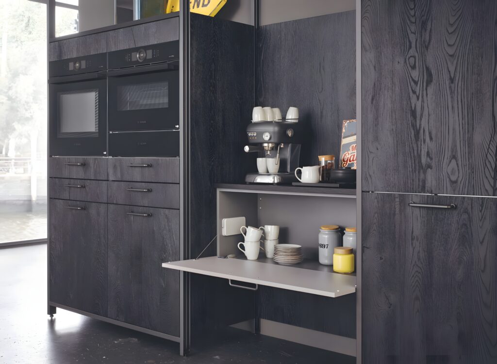 A modern kitchen setup with dark wood veneer cabinetry, built-in ovens, and a fold-out shelf displaying a coffee machine, mugs, and various containers.