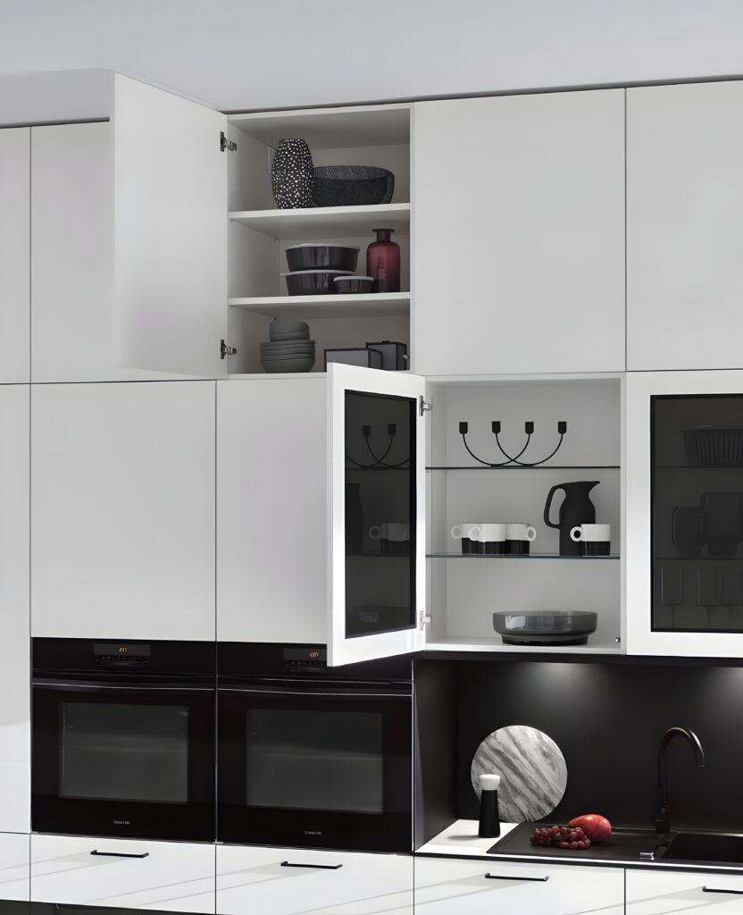 Modern kitchen with white cabinets features an ergonomic kitchen layout. Several cabinet doors are open, revealing dishes and kitchenware inside. Black double ovens are built into the cabinetry, and a black countertop runs below.