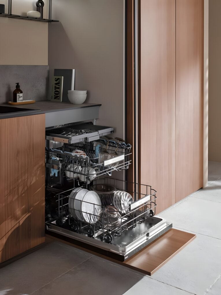 A built-in dishwasher, partially open, is fully loaded with clean dishes, including plates, bowls, and glasses. Set in a modern kitchen with wooden cabinetry and minimalist decor, it exemplifies seamless technological integration in material design.