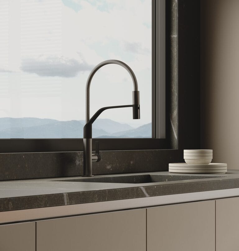 A minimalist kitchen with a modern black faucet over a grey countertop. Two white bowls are stacked beside the sink, and a large window offers a view of distant mountains.