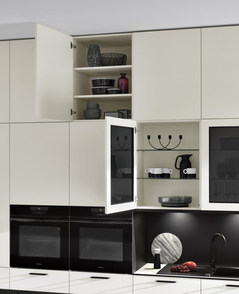 Modern kitchen with white cabinets, some of which are open for organizing cabinets for easy reach. Inside are various dishes and decorative items. Below the cabinets are two black built-in ovens and a black backsplash with decor.
