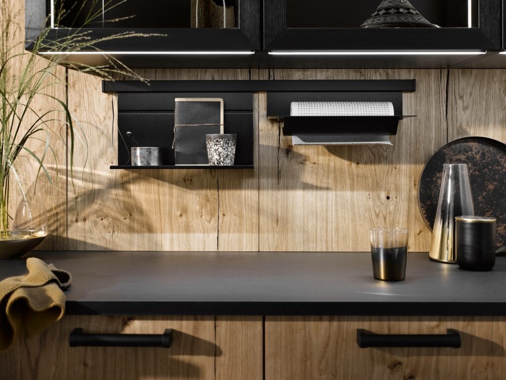 A modern kitchen with wooden walls, black cabinets, and a gray countertop designed at the perfect working height for your kitchen. Items such as a glass, containers, a towel, and a tablet are arranged on and above the counter.