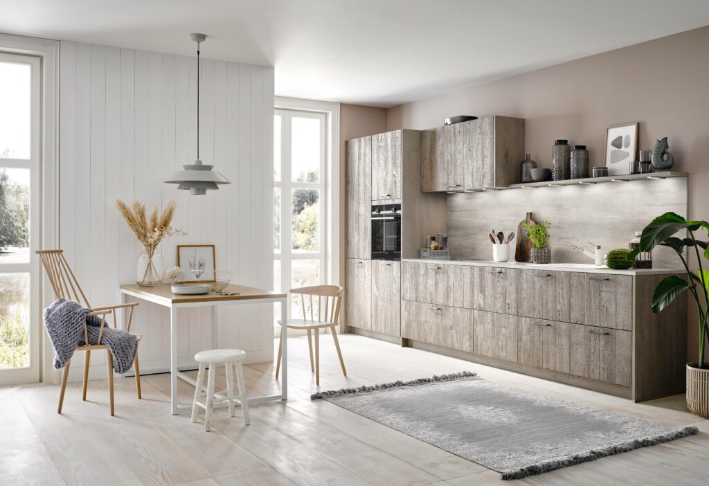 Modern kitchen with wooden cabinets, a dining table with mixed chairs, and a rug. Natural light enters through large windows. Walls are white and beige. Pendant light hangs over the dining area—perfect kitchen design for home cooks who love a functional yet stylish space.