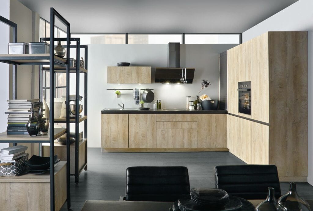 A modern kitchen with wooden cabinets, stainless steel appliances, and black accents. Shelves with books and decor items are on the left side. The kitchen is well-lit with natural and artificial light, showcasing a thoughtful design philosophy that emphasizes both aesthetics and kitchen ergonomics.