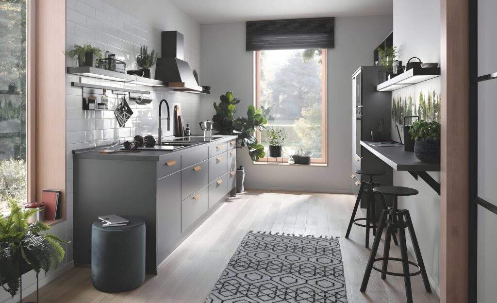 A modern kitchen with grey cabinetry, white subway tile backsplash, and a wooden floor. The space features a large window, potted plants, open shelving, and a black range hood. Embracing ergonomic kitchen designs, it includes a rug with geometric patterns for added comfort.
