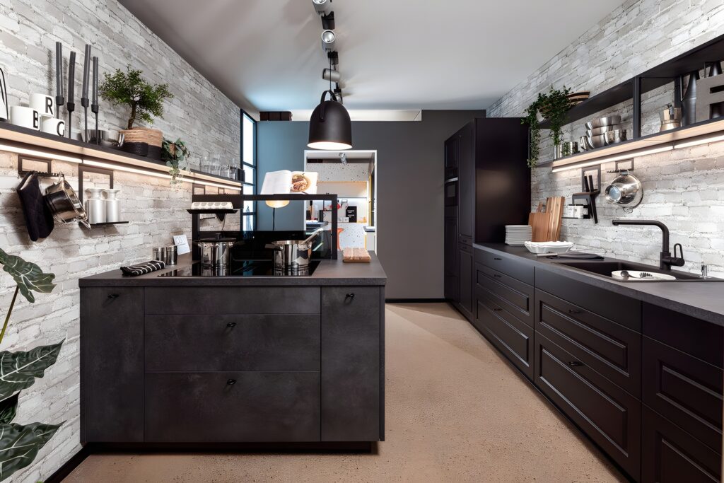 A modern kitchen with an ergonomic layout features white brick walls, dark cabinets, and countertops. Shelves hold plants and kitchenware, while a central island and pendant lights complete the streamlined space.